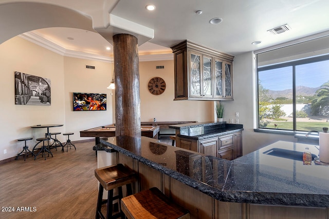 kitchen featuring hardwood / wood-style flooring, decorative columns, a breakfast bar area, crown molding, and sink