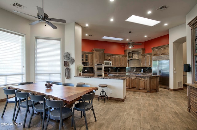 kitchen with dark stone countertops, a kitchen island, light hardwood / wood-style floors, kitchen peninsula, and built in appliances