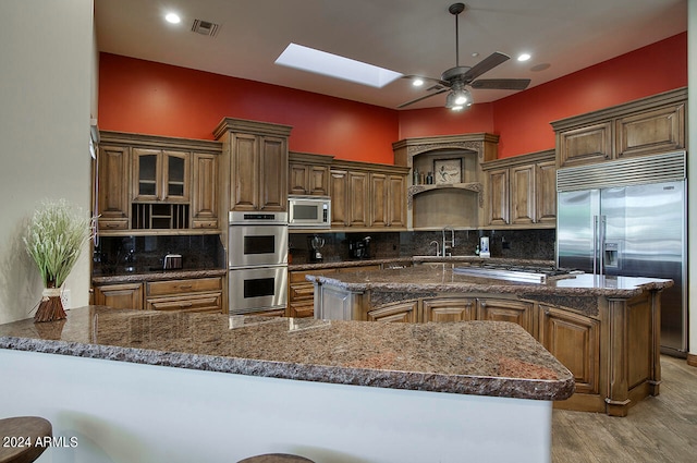 kitchen featuring a center island, kitchen peninsula, decorative backsplash, built in appliances, and light wood-type flooring