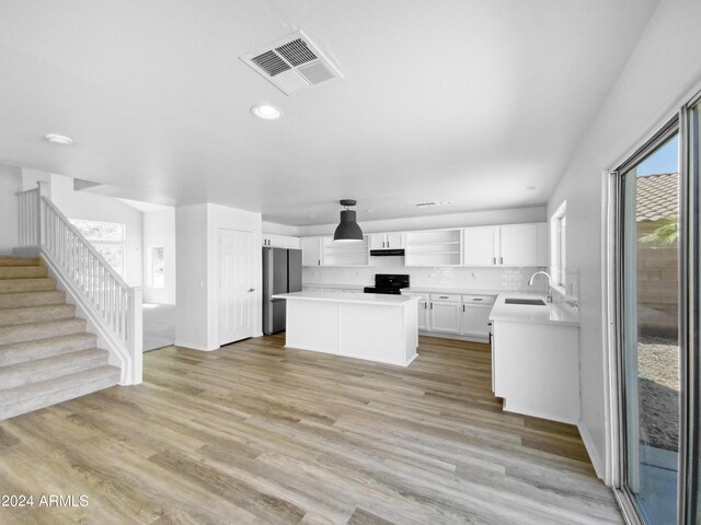 kitchen featuring white cabinetry, sink, a center island, stainless steel fridge, and light hardwood / wood-style floors