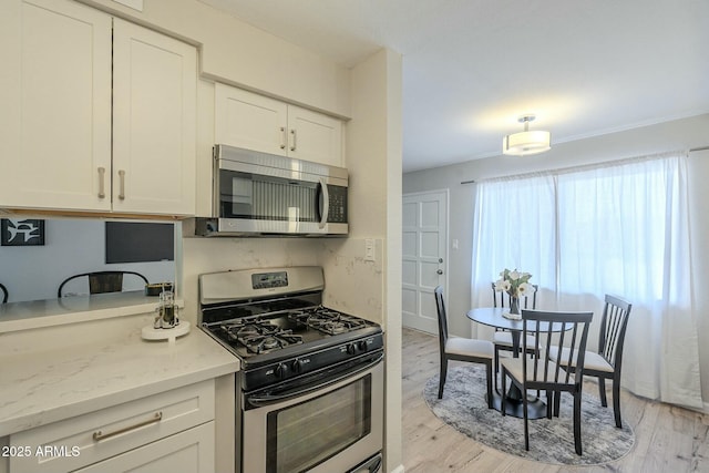 kitchen featuring light stone counters, appliances with stainless steel finishes, light wood-style flooring, and white cabinetry