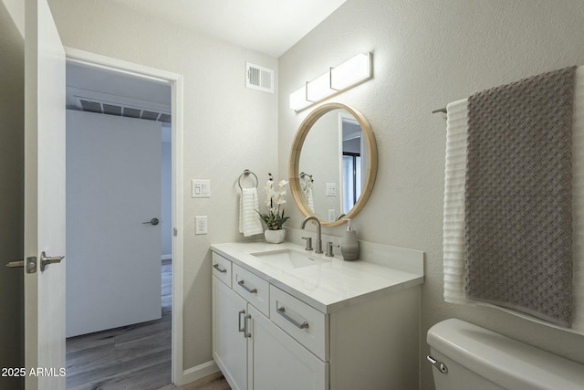 bathroom featuring visible vents, a textured wall, vanity, and toilet