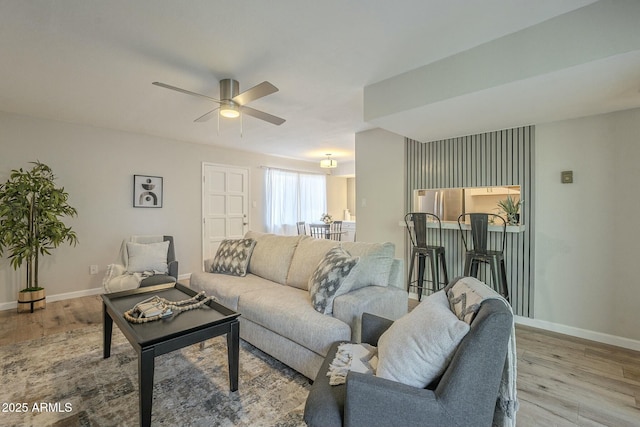 living room featuring light wood finished floors, ceiling fan, and baseboards