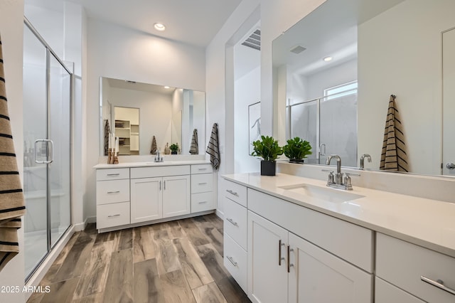 bathroom featuring two vanities, a sink, a shower stall, and wood finished floors