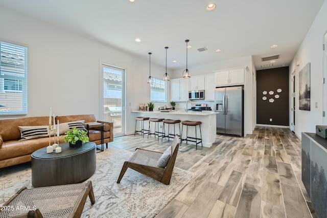 living room featuring recessed lighting, baseboards, visible vents, and light wood finished floors