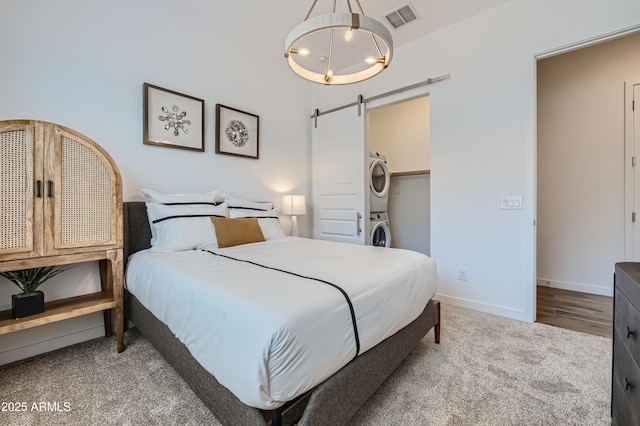 bedroom with stacked washer and dryer, visible vents, an inviting chandelier, a barn door, and baseboards