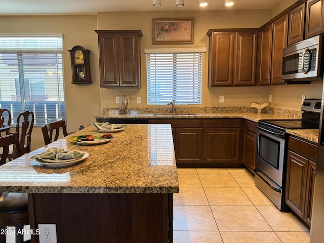 kitchen featuring a center island, light tile patterned floors, appliances with stainless steel finishes, a kitchen breakfast bar, and a sink