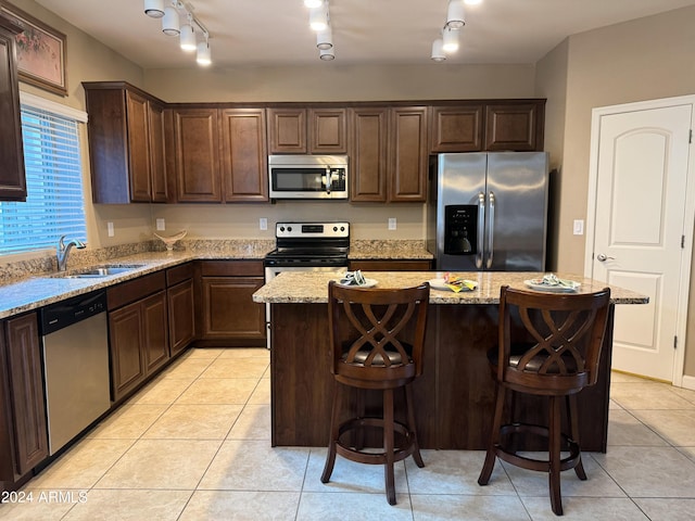 kitchen featuring a kitchen island, dark brown cabinetry, light tile patterned floors, stainless steel appliances, and a sink