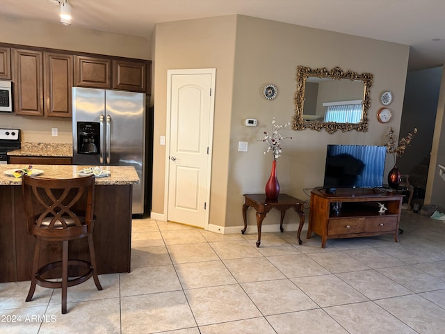 kitchen featuring baseboards, a breakfast bar area, light tile patterned floors, light stone counters, and stainless steel appliances