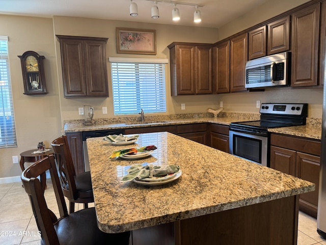 kitchen featuring light tile patterned floors, a breakfast bar, a sink, stainless steel appliances, and dark brown cabinets