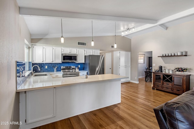 kitchen with a peninsula, wood finished floors, a sink, light countertops, and appliances with stainless steel finishes