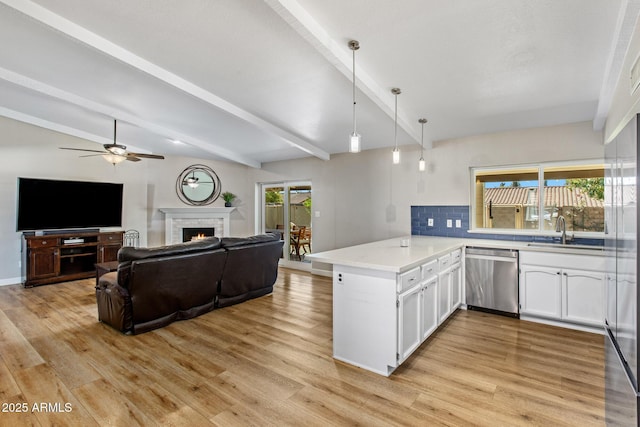 kitchen with stainless steel dishwasher, white cabinetry, a sink, a warm lit fireplace, and a peninsula