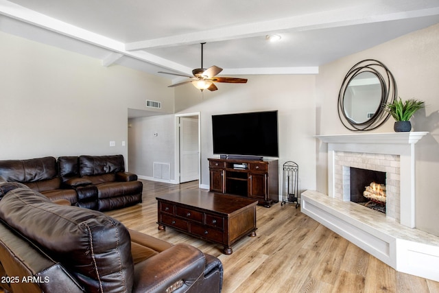 living room with light wood-type flooring, a brick fireplace, visible vents, and vaulted ceiling with beams