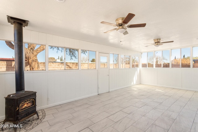 unfurnished sunroom with ceiling fan and a wood stove