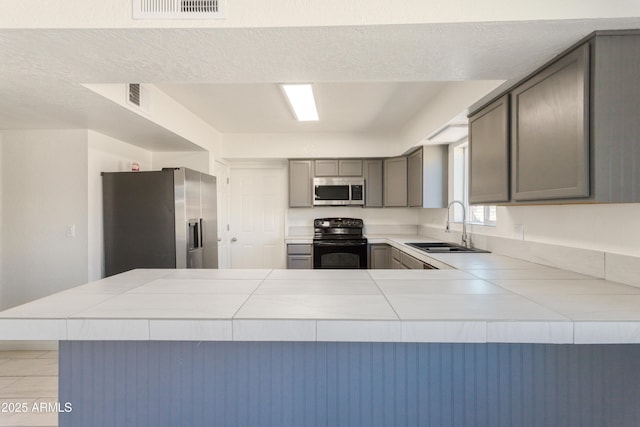 kitchen featuring appliances with stainless steel finishes, tile countertops, kitchen peninsula, and sink