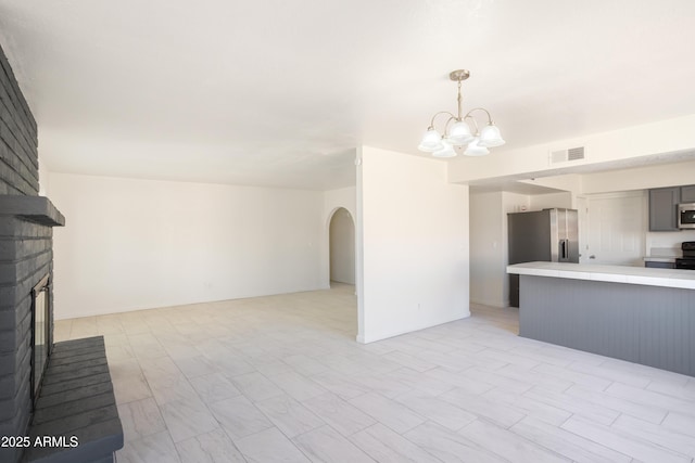 kitchen with gray cabinetry, a chandelier, hanging light fixtures, appliances with stainless steel finishes, and a fireplace