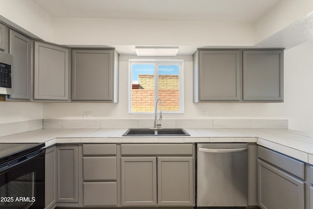 kitchen featuring gray cabinets, sink, stainless steel dishwasher, tile counters, and black electric range