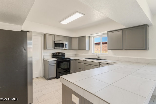 kitchen with sink, gray cabinetry, tile counters, kitchen peninsula, and stainless steel appliances