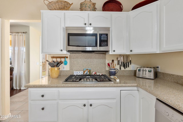 kitchen with appliances with stainless steel finishes, light stone counters, white cabinets, and light tile patterned flooring