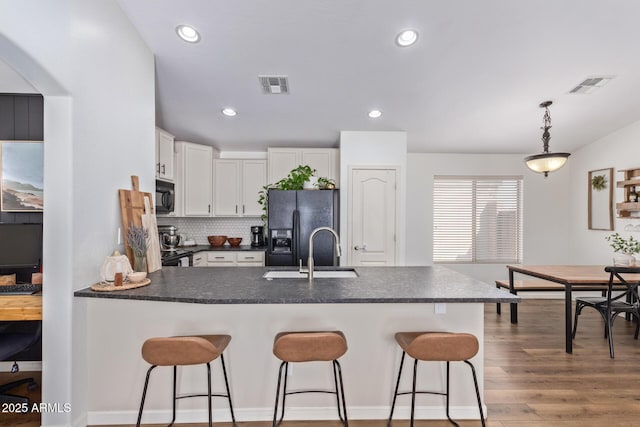 kitchen featuring sink, decorative light fixtures, white cabinets, light hardwood / wood-style floors, and black appliances