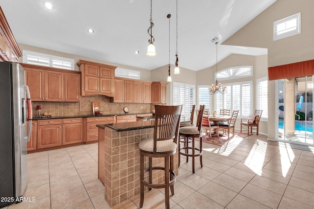 kitchen featuring tasteful backsplash, stainless steel refrigerator with ice dispenser, a chandelier, decorative light fixtures, and a kitchen island with sink