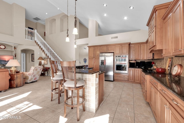 kitchen with decorative backsplash, appliances with stainless steel finishes, a towering ceiling, light tile patterned floors, and decorative light fixtures