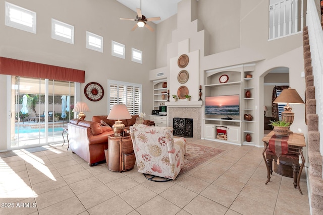 living room with built in shelves, light tile patterned flooring, a towering ceiling, and ceiling fan