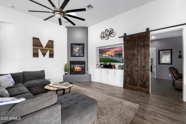 living room with visible vents, a barn door, dark wood-type flooring, a large fireplace, and ceiling fan