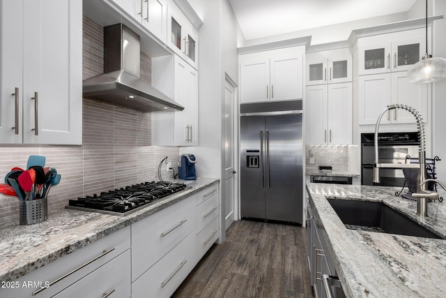 kitchen with appliances with stainless steel finishes, dark wood-type flooring, wall chimney range hood, and white cabinetry