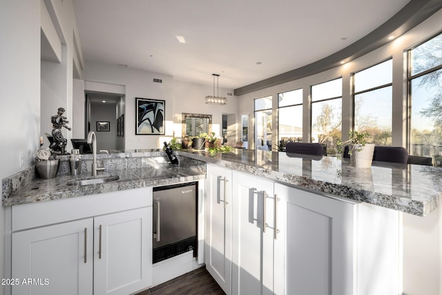 kitchen with pendant lighting, dark wood-type flooring, freestanding refrigerator, white cabinetry, and a sink