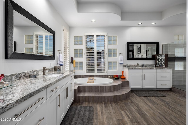 full bath with wood finished floors, two vanities, a sink, and a bath