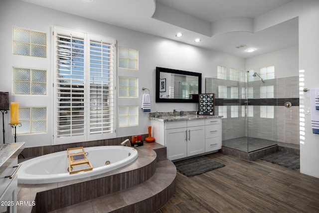 full bath featuring visible vents, tiled shower, wood finished floors, a jetted tub, and vanity