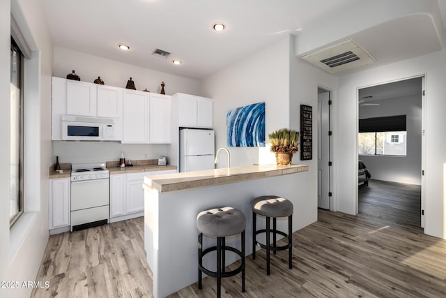 kitchen with white appliances, visible vents, light wood finished floors, and white cabinets