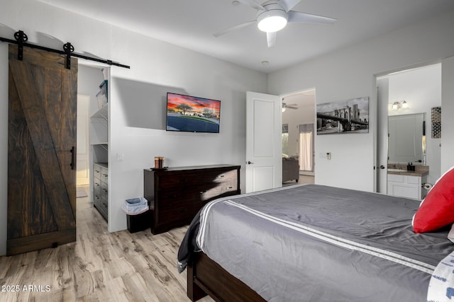 bedroom featuring light wood-type flooring, ensuite bath, and a barn door