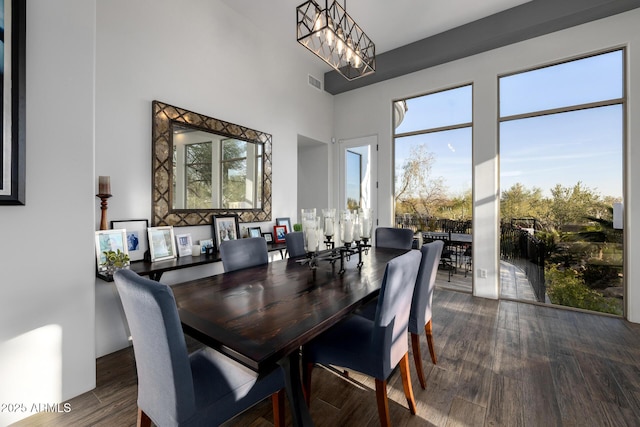 dining area with a towering ceiling, wood finished floors, visible vents, and an inviting chandelier