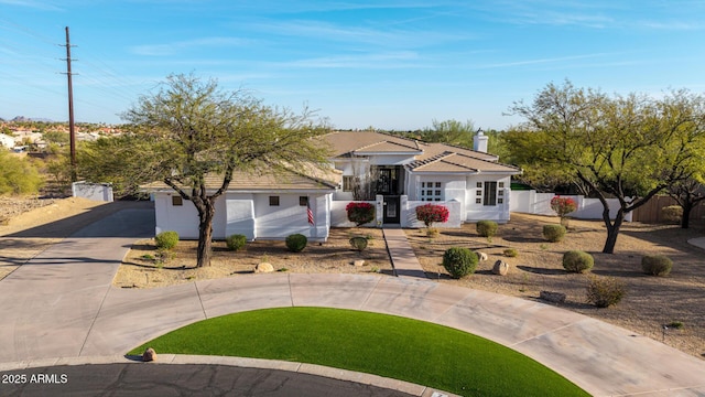 view of front of property with a tile roof, a chimney, stucco siding, concrete driveway, and fence