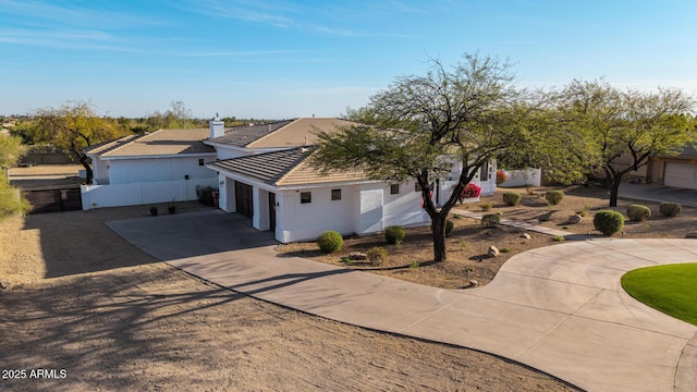 view of front facade with a garage, a tile roof, fence, concrete driveway, and stucco siding