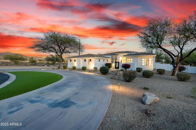 view of front facade featuring curved driveway, fence, and a front lawn