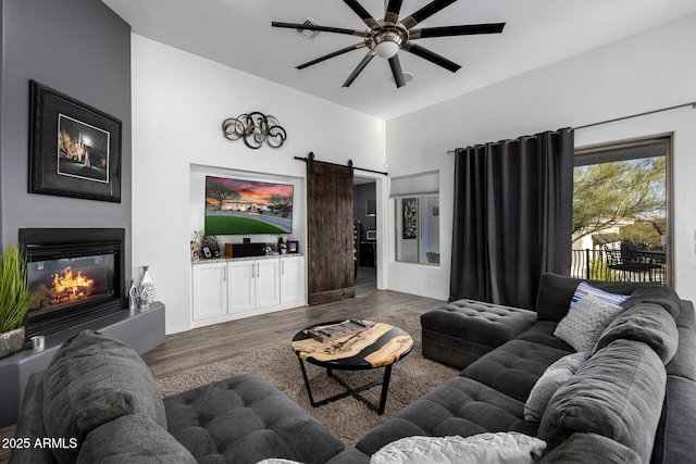 living area featuring a glass covered fireplace, wood finished floors, ceiling fan, and a barn door