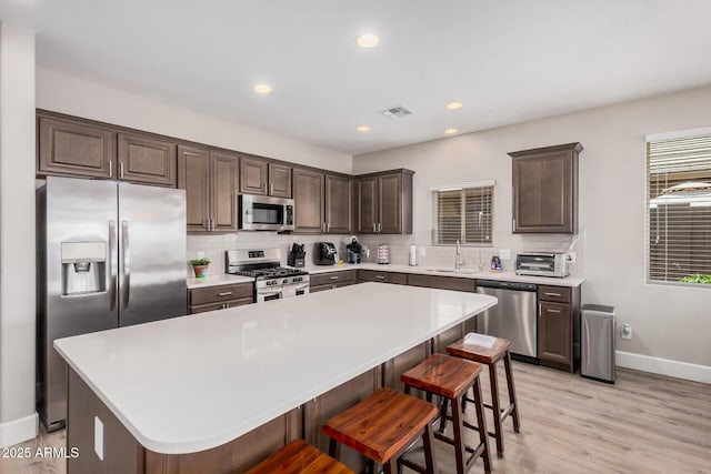 kitchen with stainless steel appliances, backsplash, dark brown cabinets, a sink, and baseboards