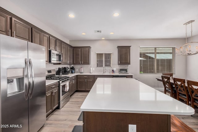 kitchen featuring an inviting chandelier, dark brown cabinetry, stainless steel appliances, light wood finished floors, and light countertops