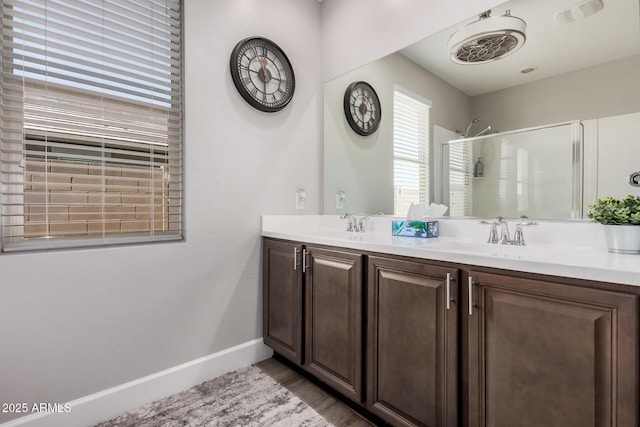 full bath featuring double vanity, wood finished floors, a sink, baseboards, and walk in shower