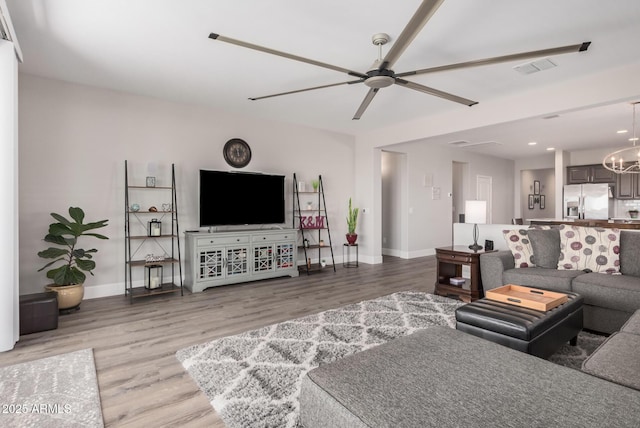 living area with ceiling fan with notable chandelier, baseboards, visible vents, and light wood finished floors