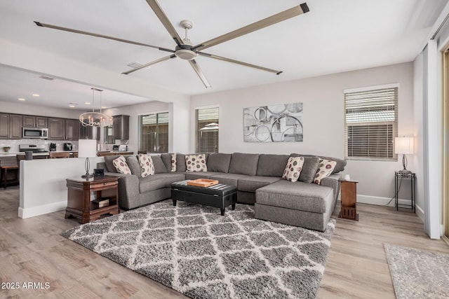 living room with ceiling fan with notable chandelier, baseboards, and light wood-type flooring