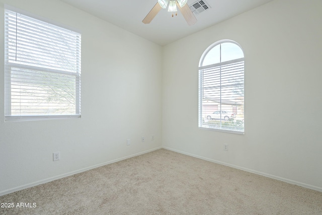 carpeted spare room featuring a ceiling fan, visible vents, and a wealth of natural light