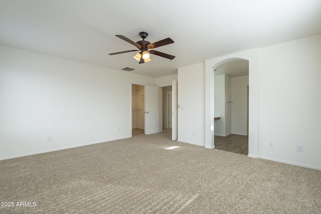 unfurnished bedroom featuring arched walkways, a walk in closet, carpet, visible vents, and baseboards