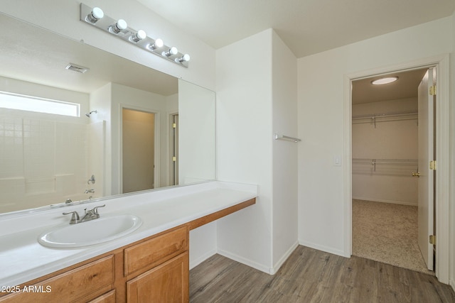 full bath with baseboards, visible vents, wood finished floors, a walk in closet, and vanity