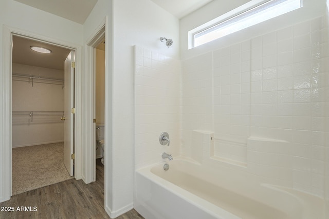 full bath with a walk in closet, toilet, washtub / shower combination, wood finished floors, and baseboards