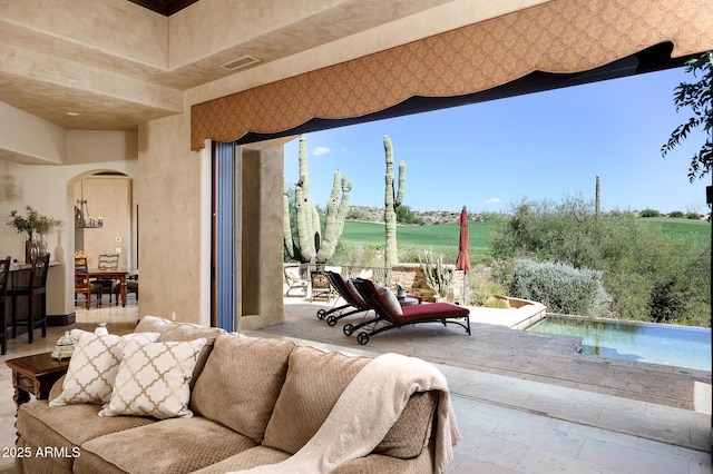 living area with view of golf course, visible vents, arched walkways, and stone tile floors