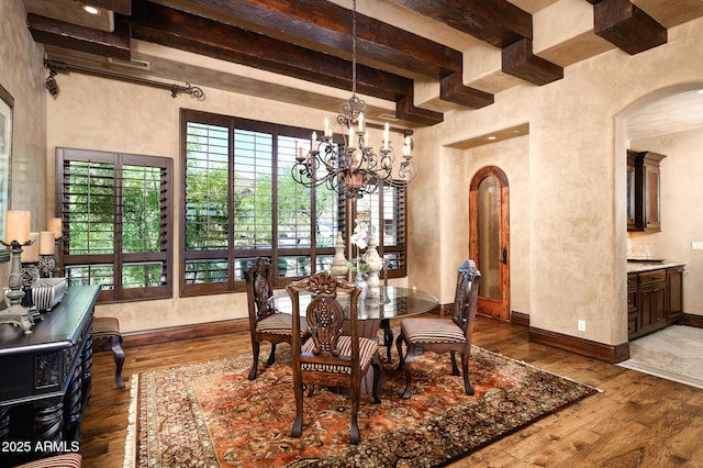 dining room featuring wood-type flooring, beamed ceiling, arched walkways, a notable chandelier, and baseboards